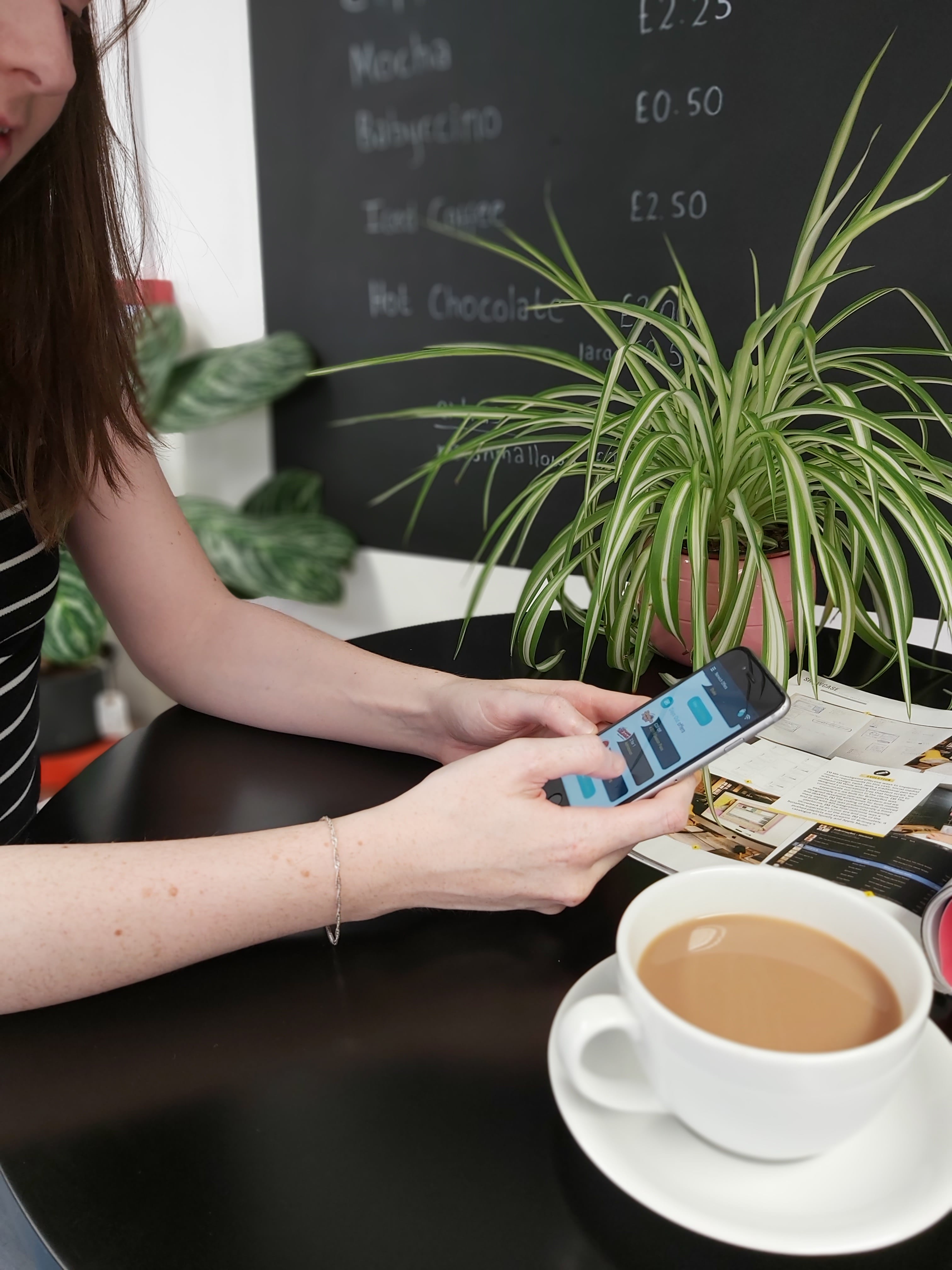 woman holding phone with Spot on Savings app on display whilst sat at a coffee table with a cup of tea in front of her